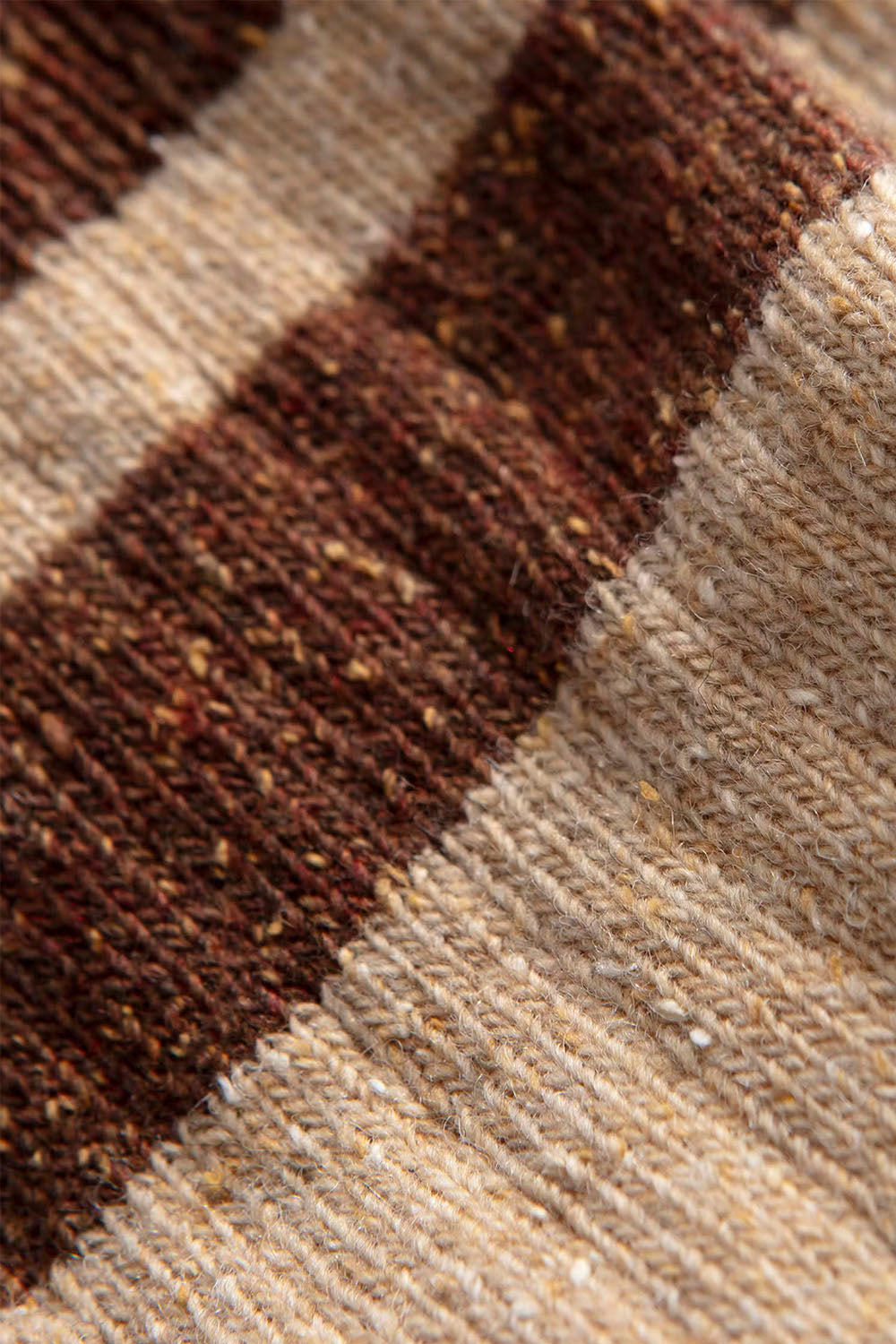 Close-up of a knit textile with horizontal stripes in dark brown and warm beige, showing the woven texture and flecks in the yarn.
