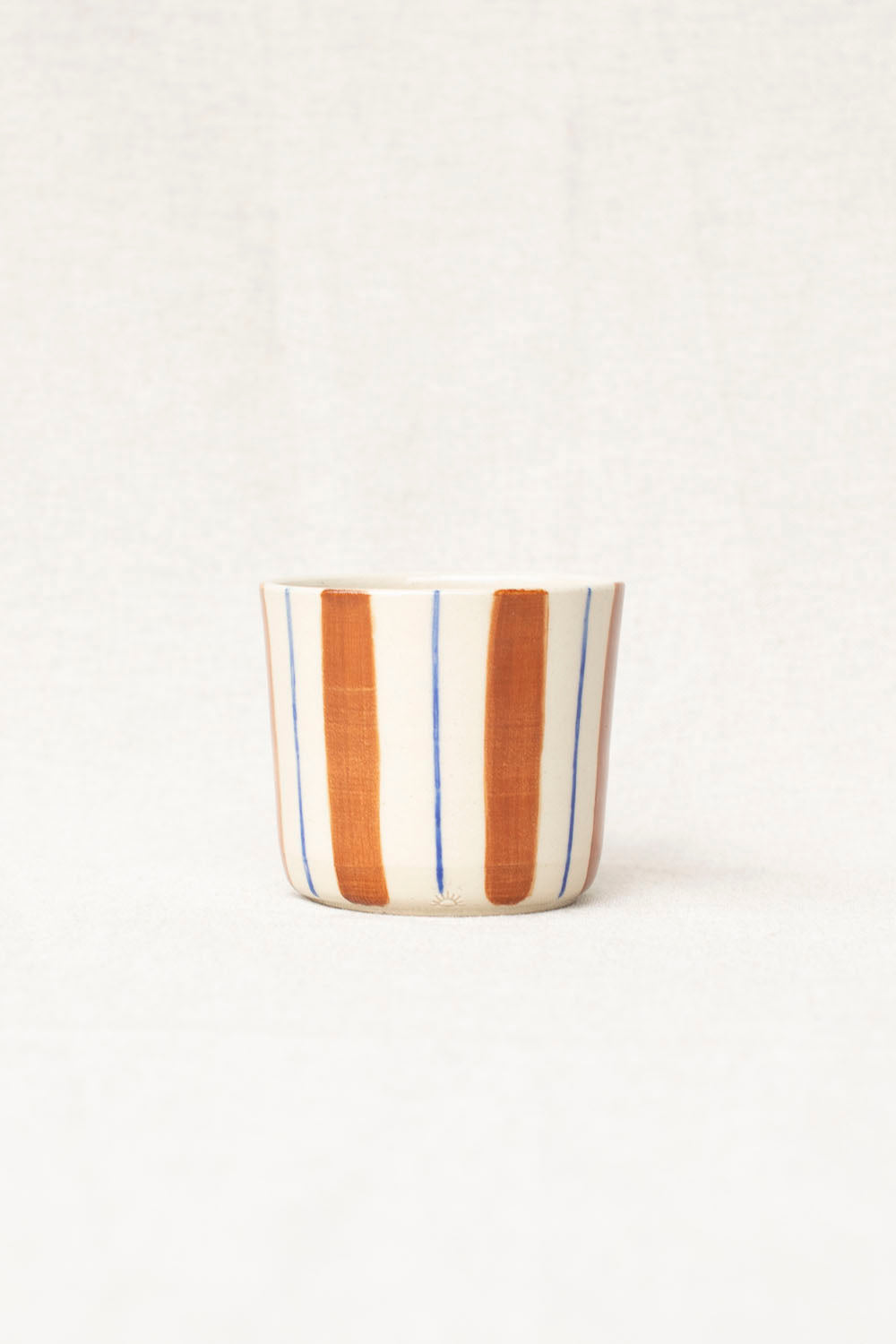 Striped ceramic cup with brown, blue, and white stripes on a white background