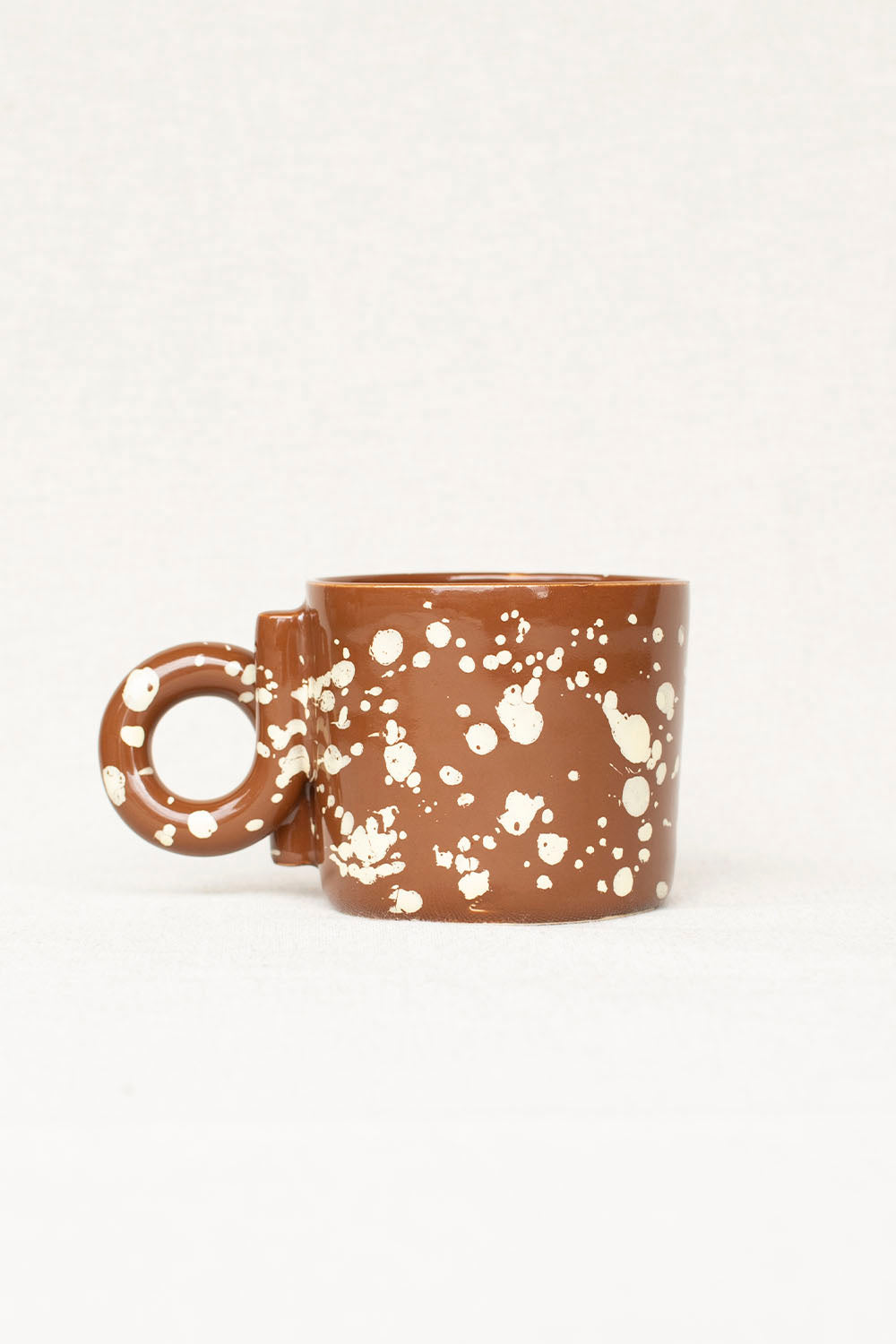 Brown ceramic mug with white speckles on a white background