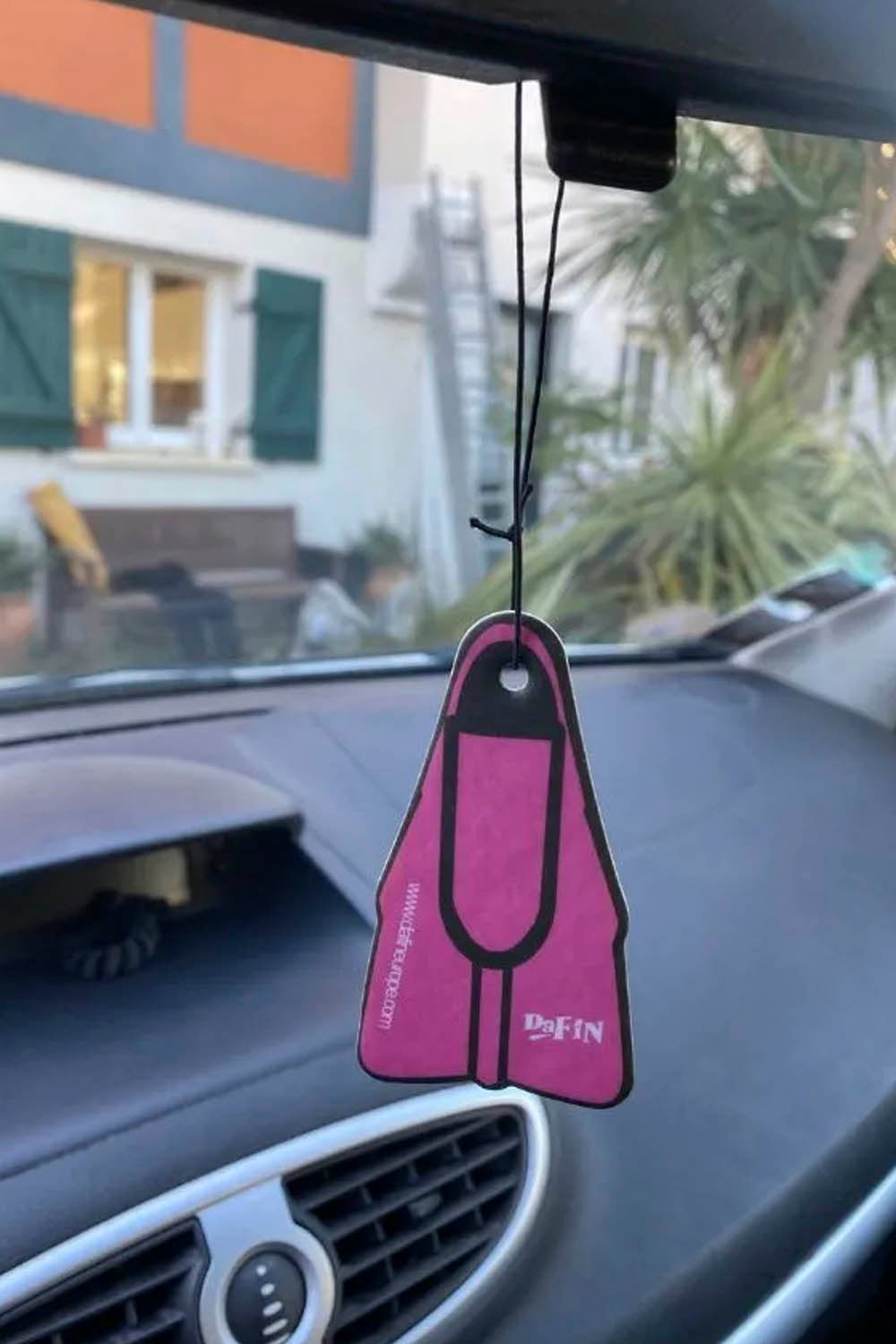 Pink flipper-shaped air freshener hanging from a car's rearview mirror.