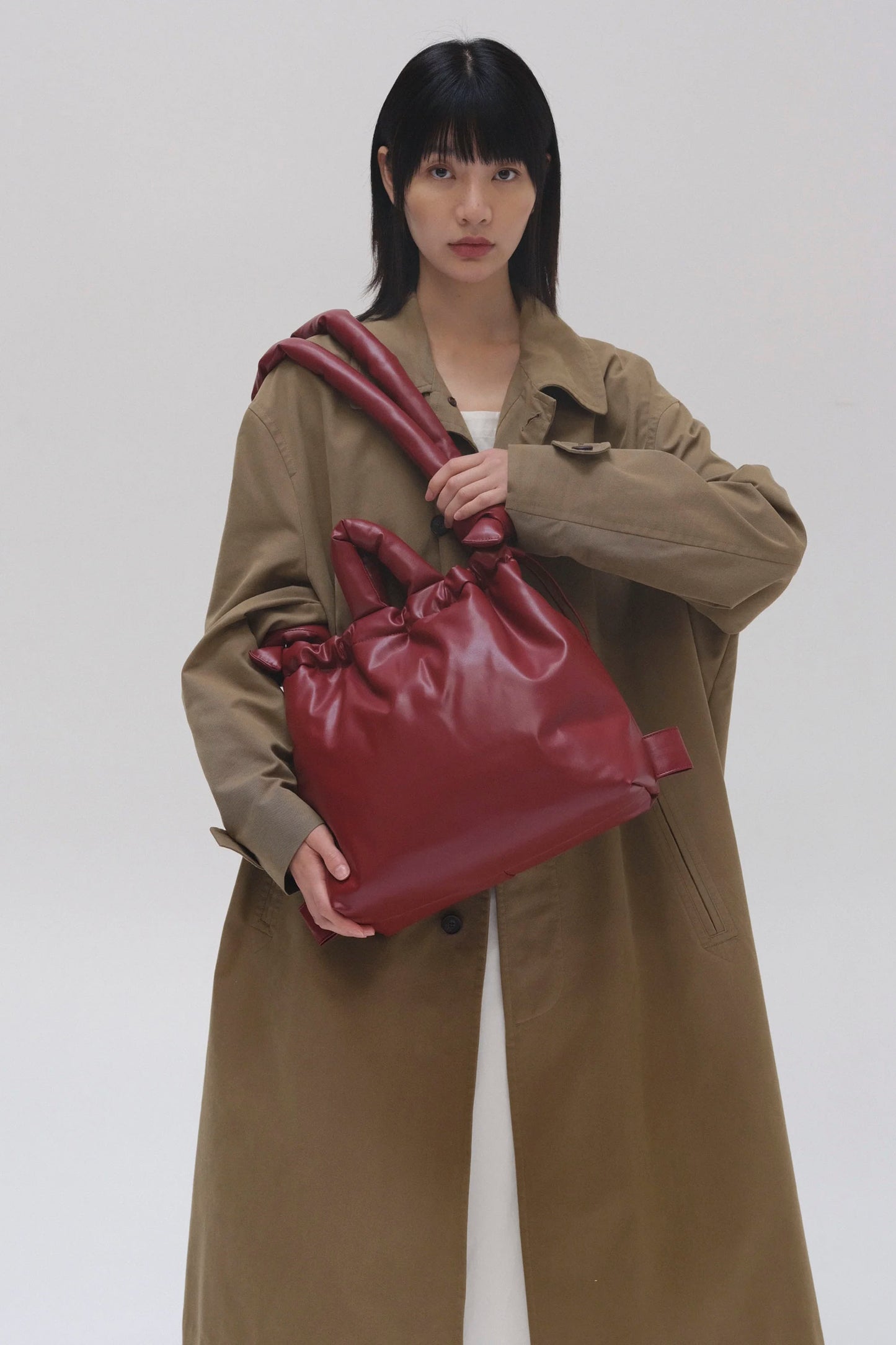 Person wearing a brown coat holding a ÖLEND Ona vegan leather bag in cherry red  against a white background