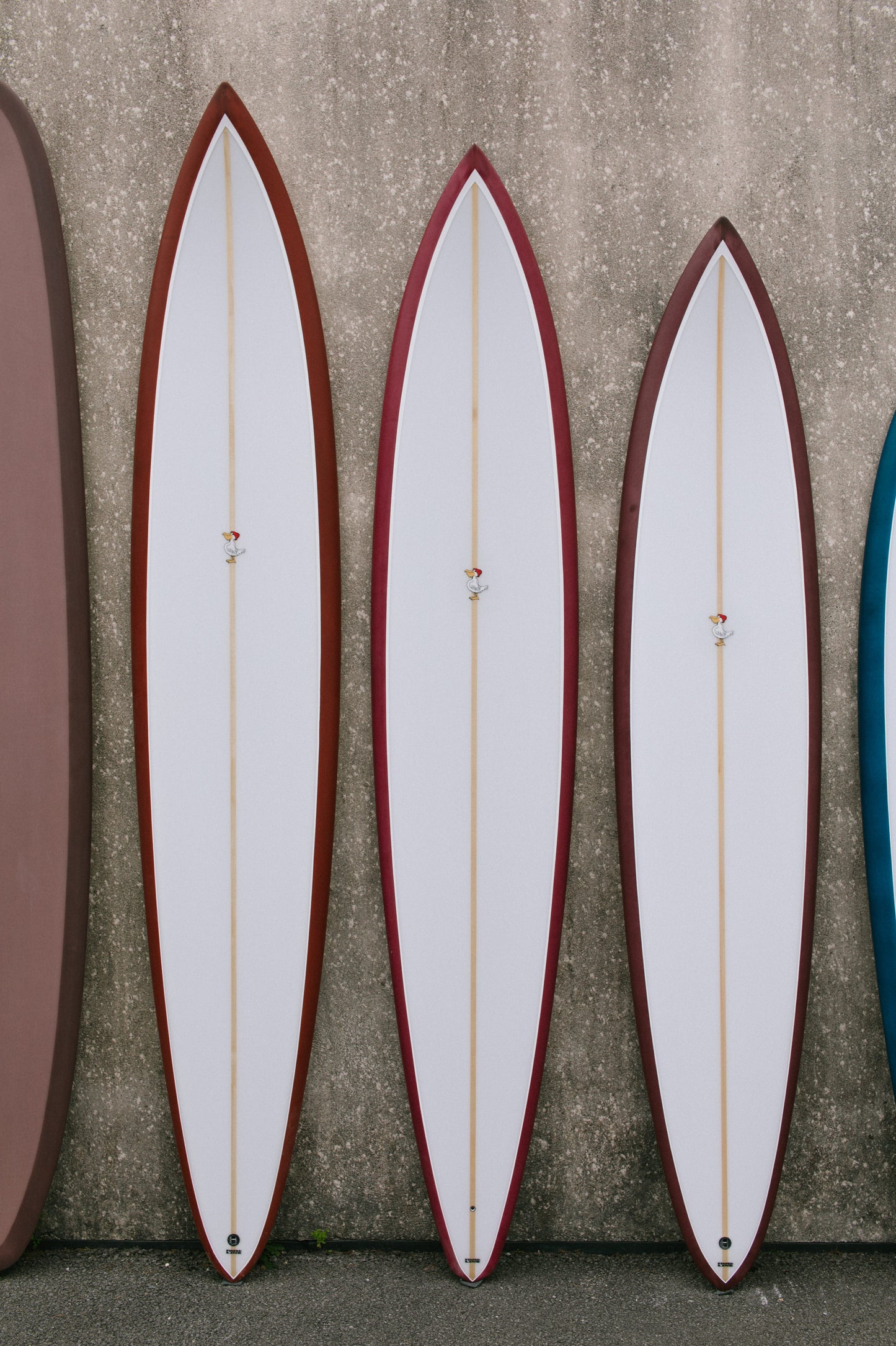 Three surfboards with red accents leaning against a textured wall.