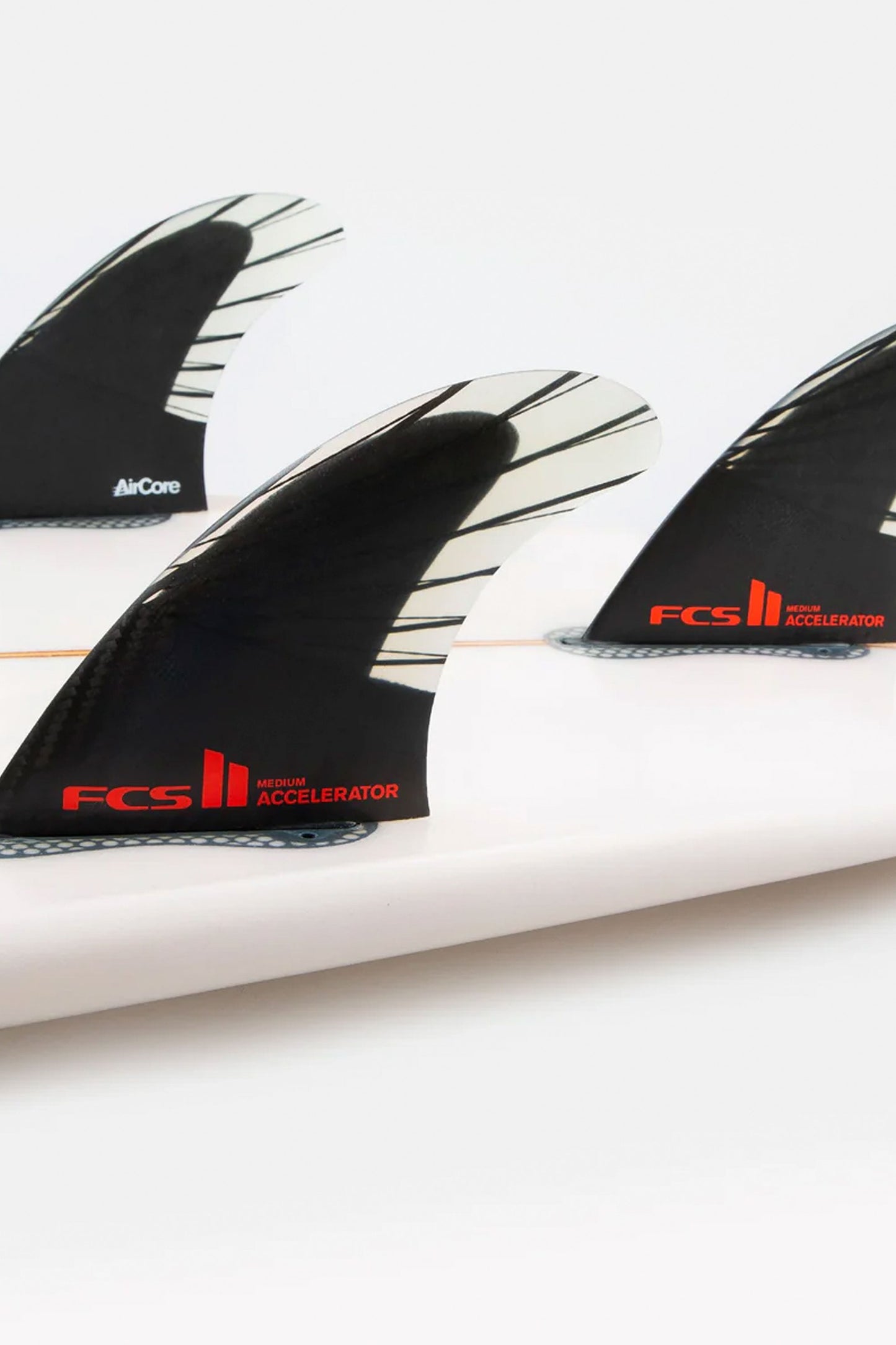 Surfboard with the FCS II Accelerator PC Carbon tri fin set on white background.