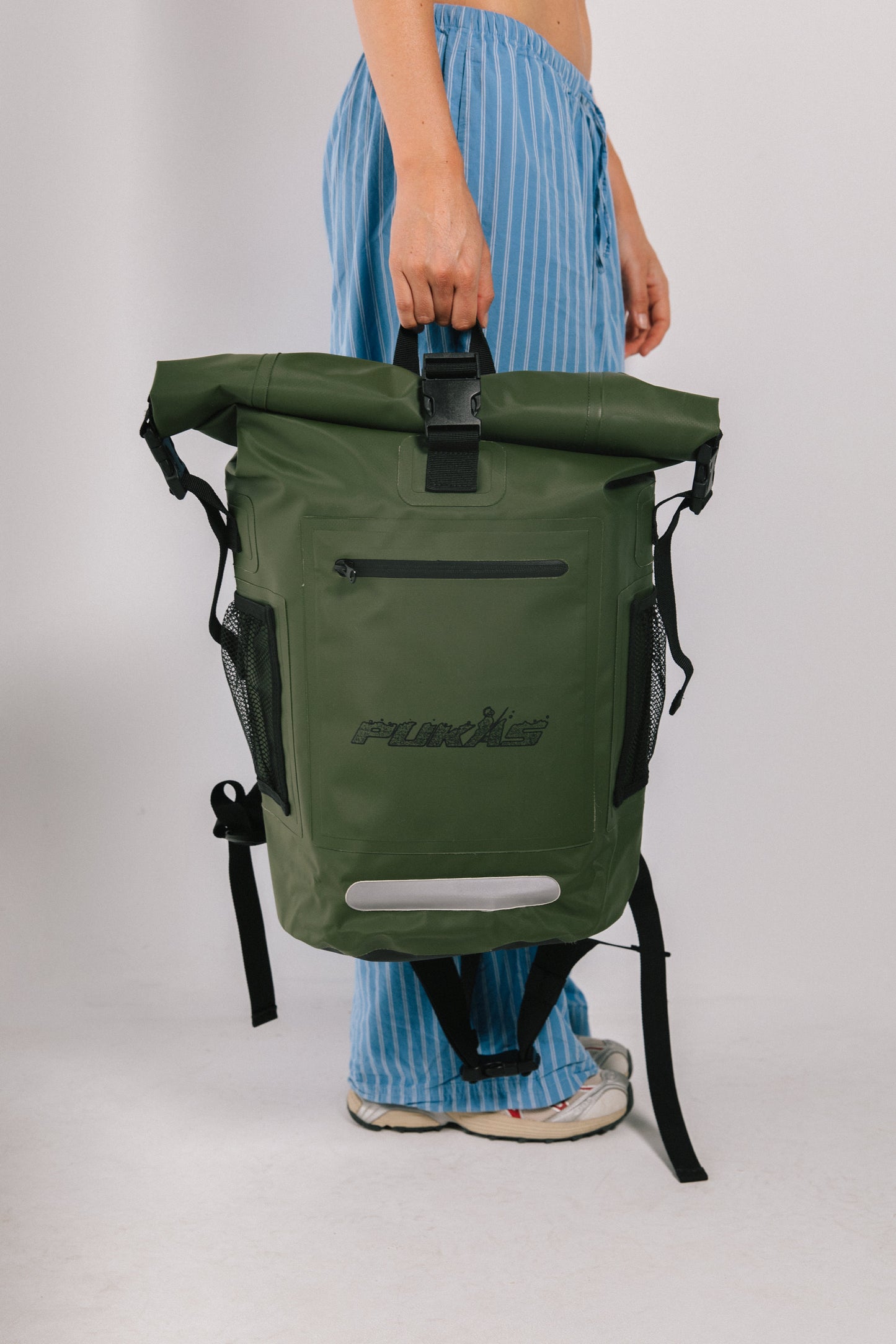 Green backpack with a visible brand logo held by a person wearing blue striped pants on a white background