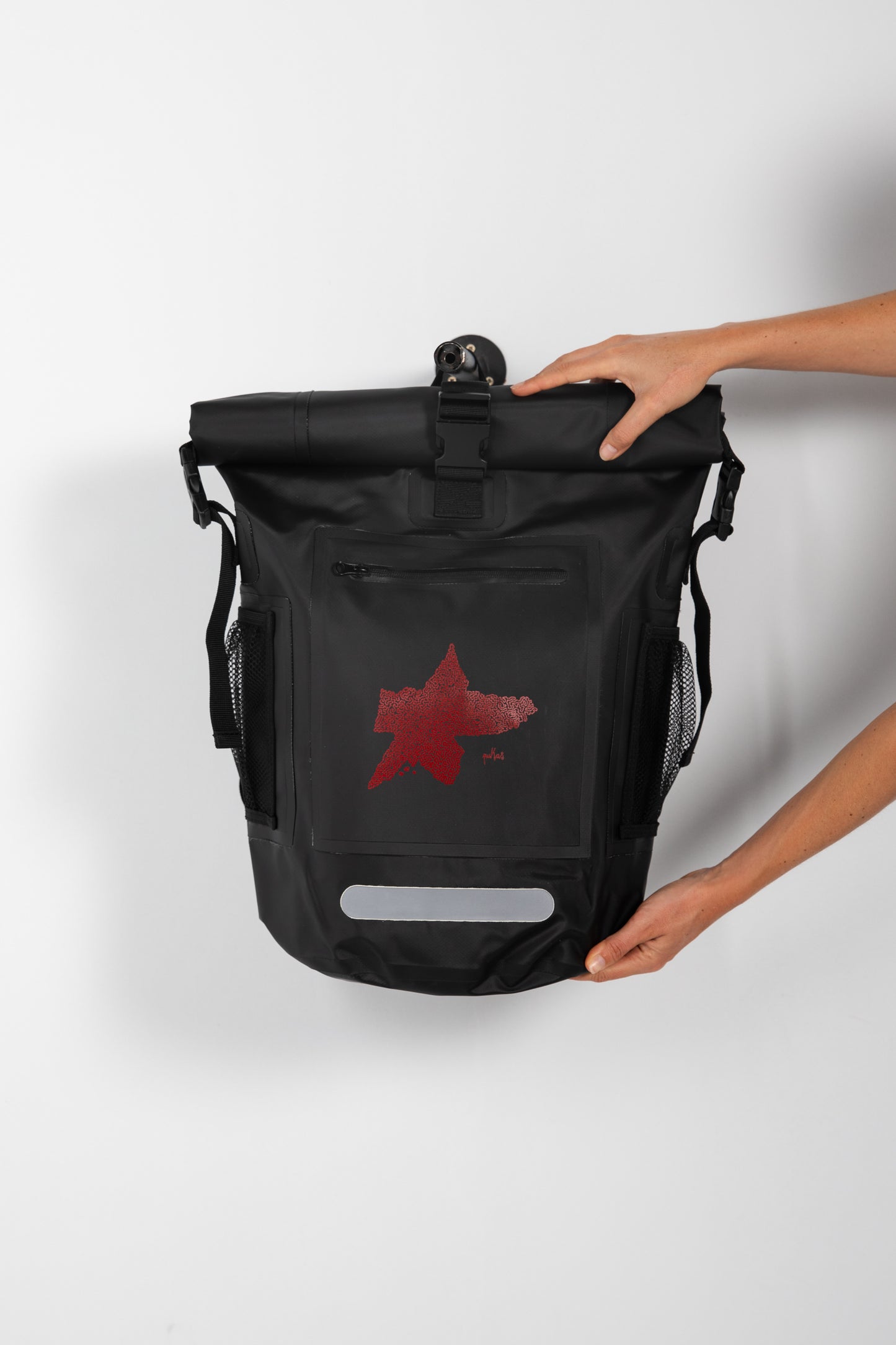 Black backpack with a red star design held by a person on a light gray background