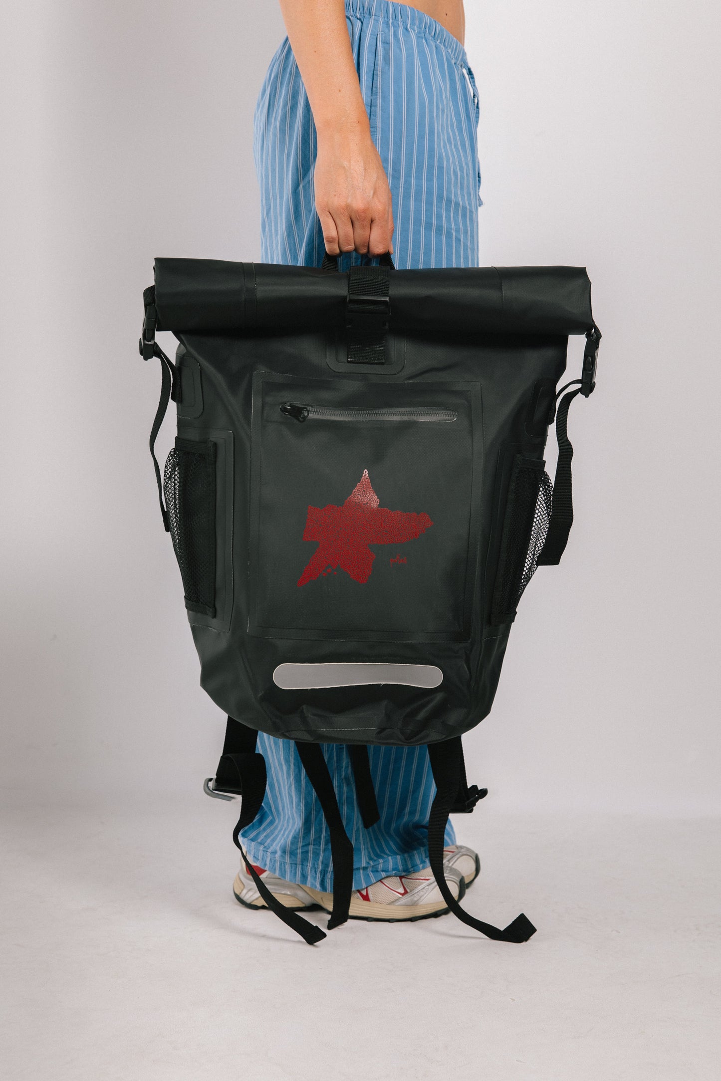 Person holding a black backpack with a red logo on a white background