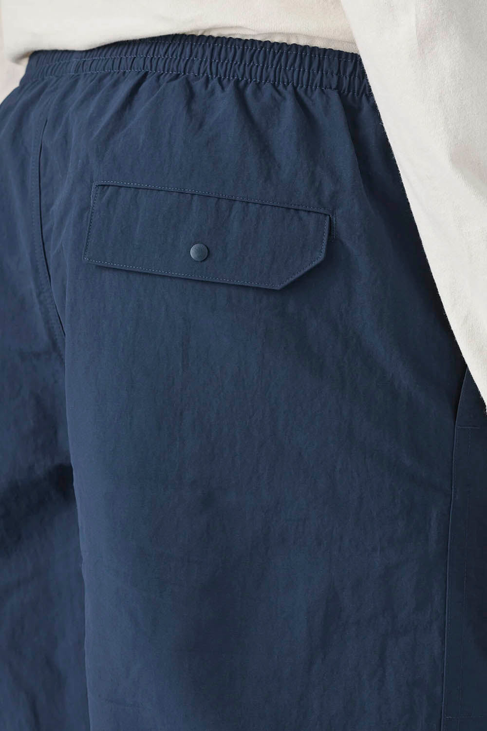A close-up back view of a person wearing navy blue shorts and a light cream long-sleeve shirt against a plain white background.
