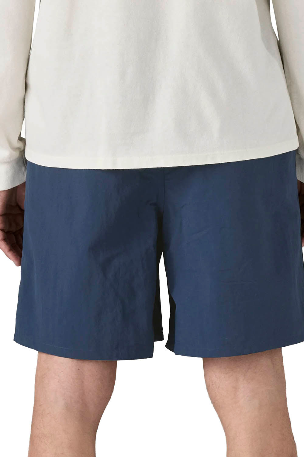 A close-up back view of a person wearing navy blue shorts and a light cream long-sleeve shirt against a plain white background.