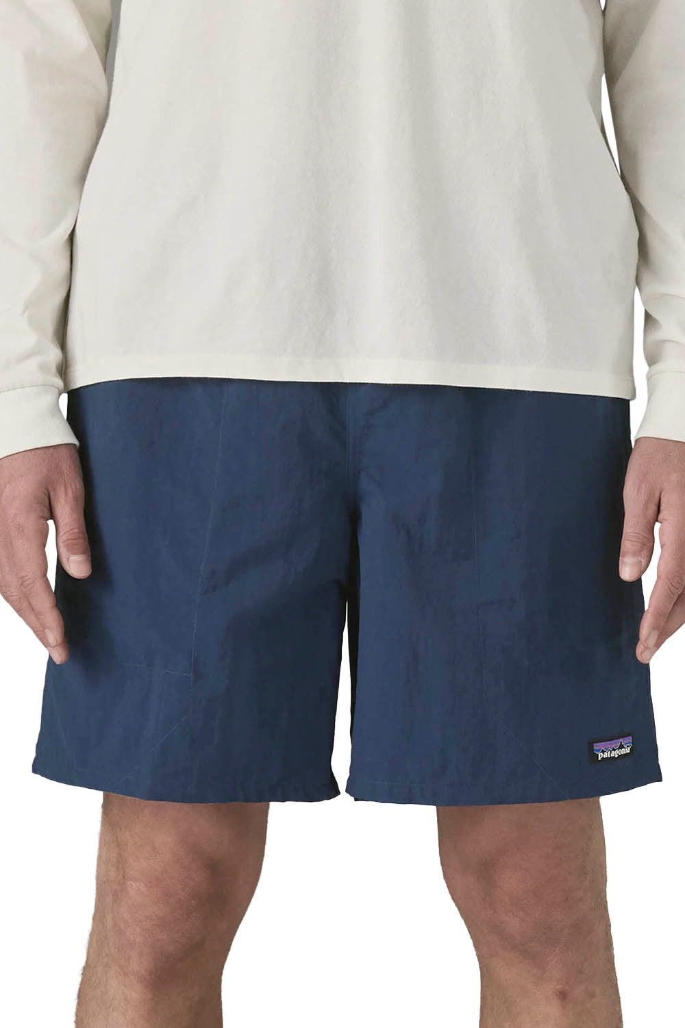 A person wearing navy blue Patagonia shorts and a light cream long-sleeve shirt, cropped from the chest to the upper thighs against a plain white background.