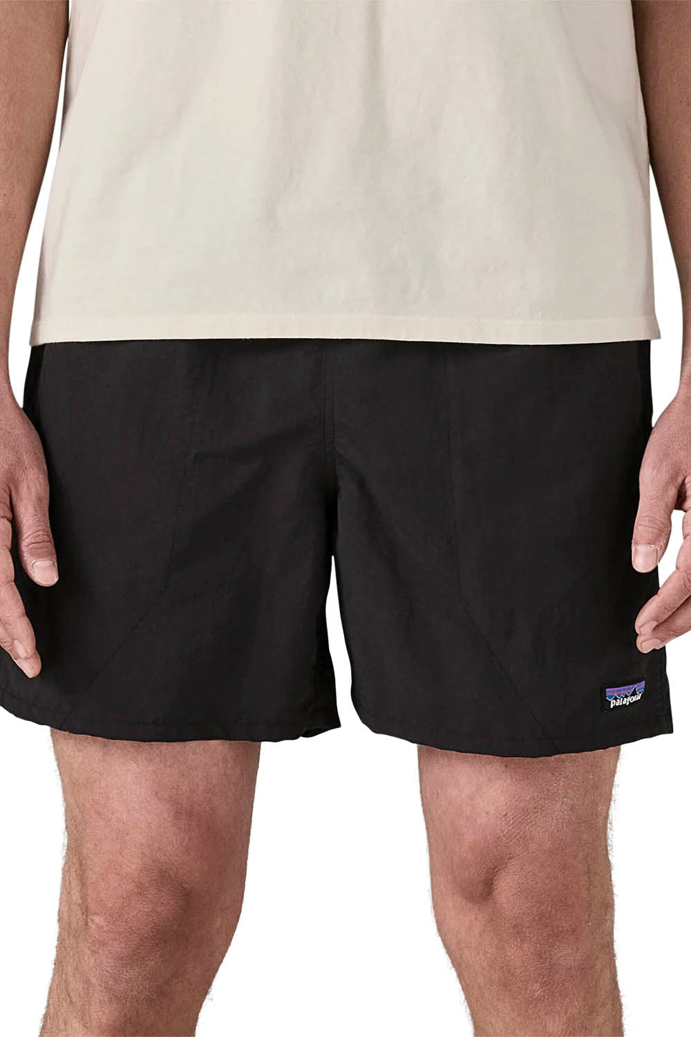 A close-up of a person wearing black Patagonia shorts and a light beige t-shirt, cropped from the chest down against a white background.