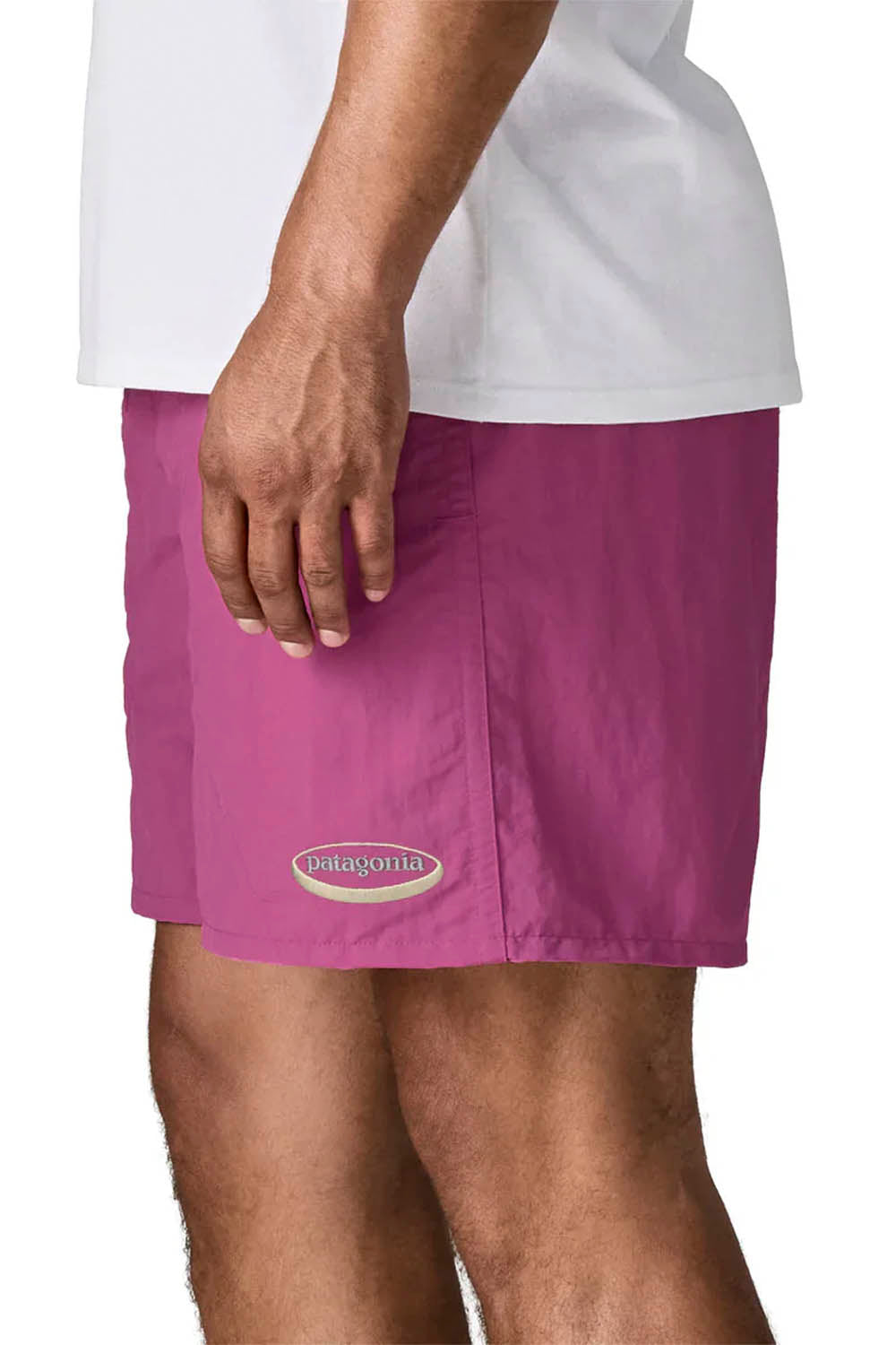 A close-up of a person wearing Patagonia shorts in a muted magenta-purple color, paired with a white t-shirt. The Patagonia logo is visible on the lower left of the shorts.