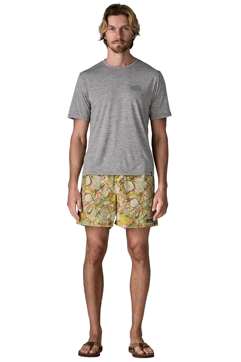 A man modeling a heather gray crewneck t-shirt and patterned swim shorts with a tropical floral print in yellow, green, and orange, paired with brown sandals, against a plain white background.