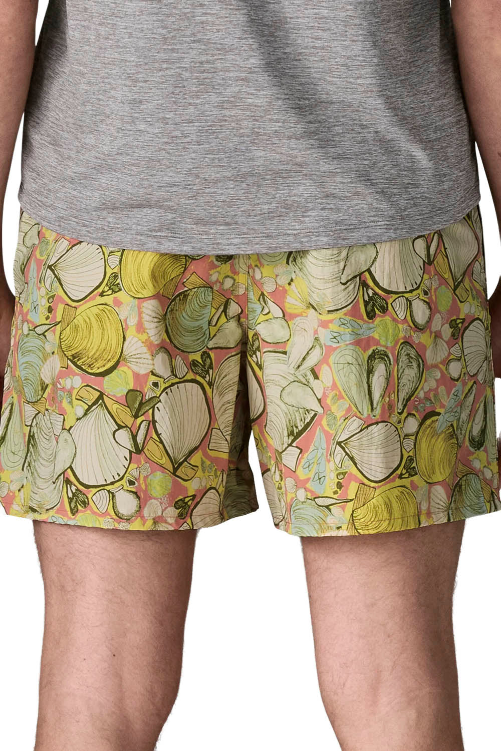 A close-up of a person wearing patterned swim shorts with a seashell design in yellow, green, and pink, paired with a gray heathered t-shirt.