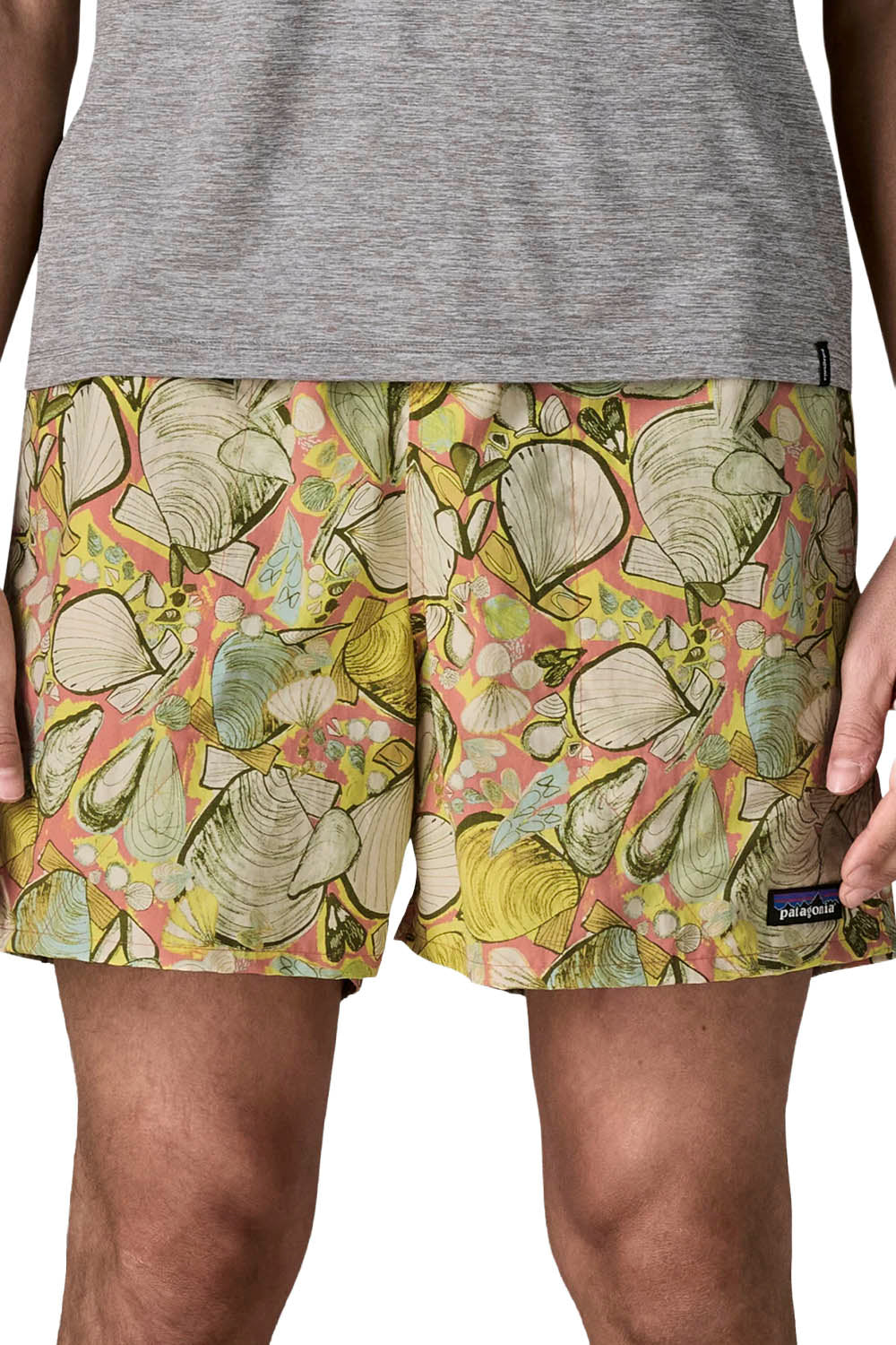 Men's swim trunks featuring a colorful seashell pattern in yellow, green, and pink, worn by a model with a gray t-shirt visible at the top.