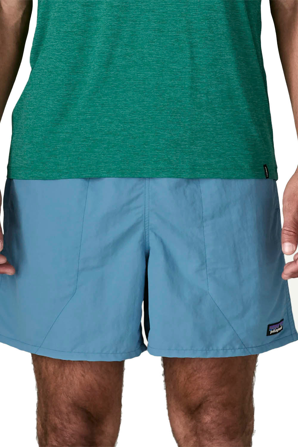 A close-up of a person wearing light blue Patagonia board shorts and a green heathered tank top against a plain white background.
