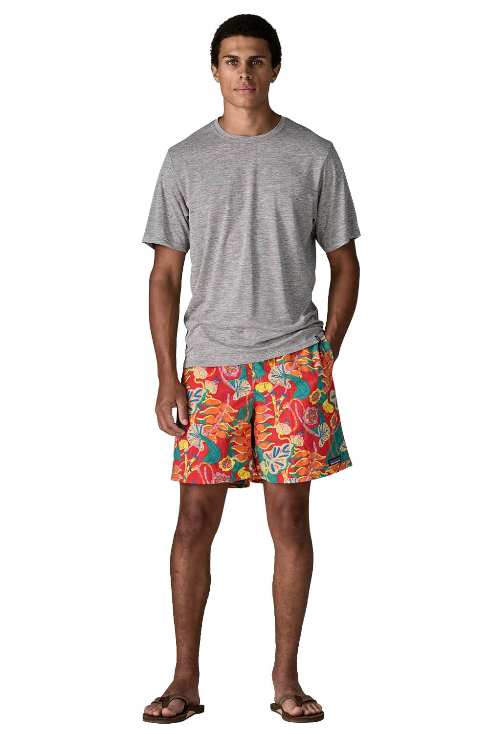 A man modeling a heather gray crewneck t-shirt and vibrant, multicolor tropical print swim shorts against a plain white background.