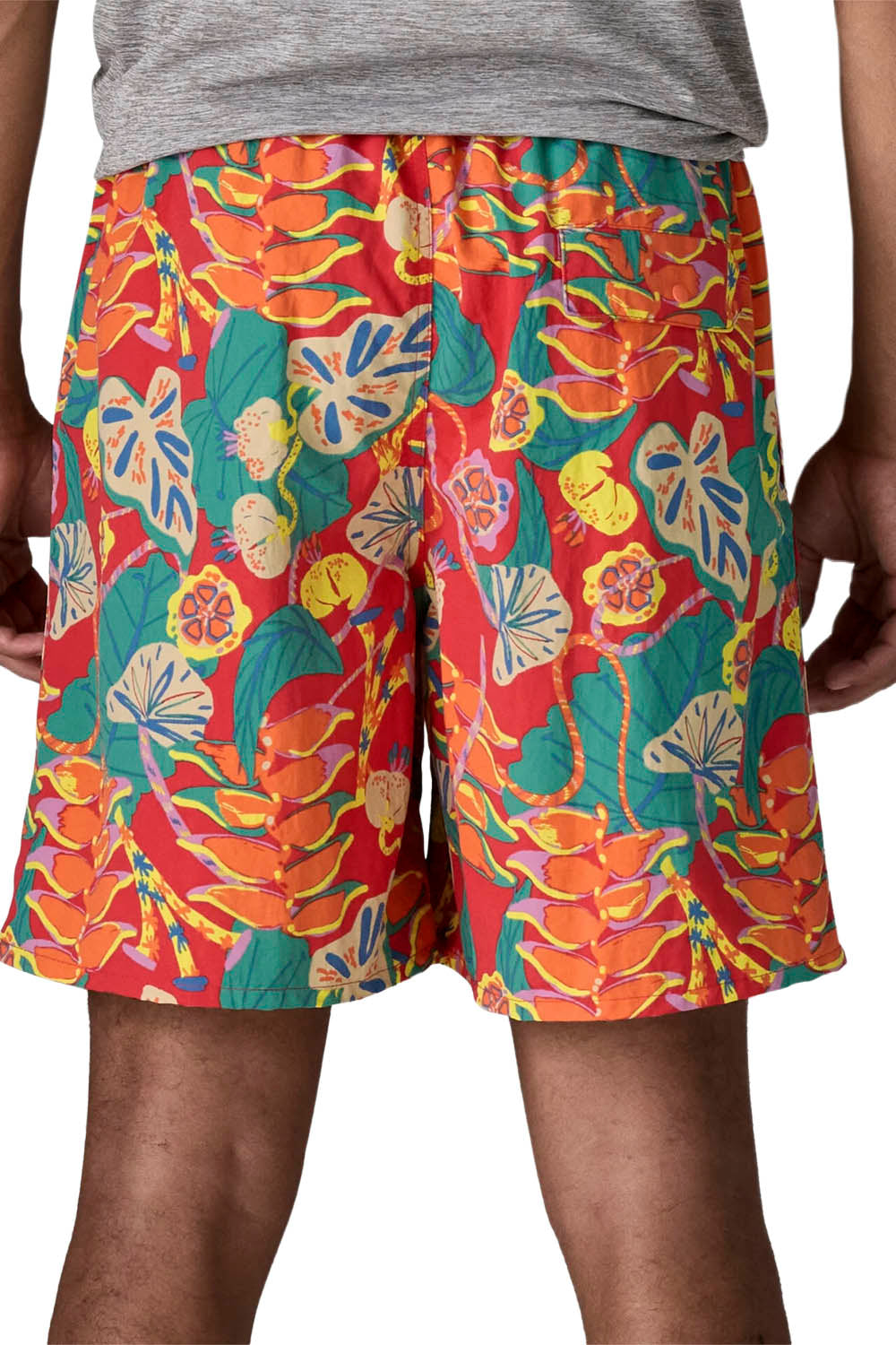 A close-up of a person wearing colorful tropical print shorts with a gray t-shirt partially visible, shown from the waist down against a white background.