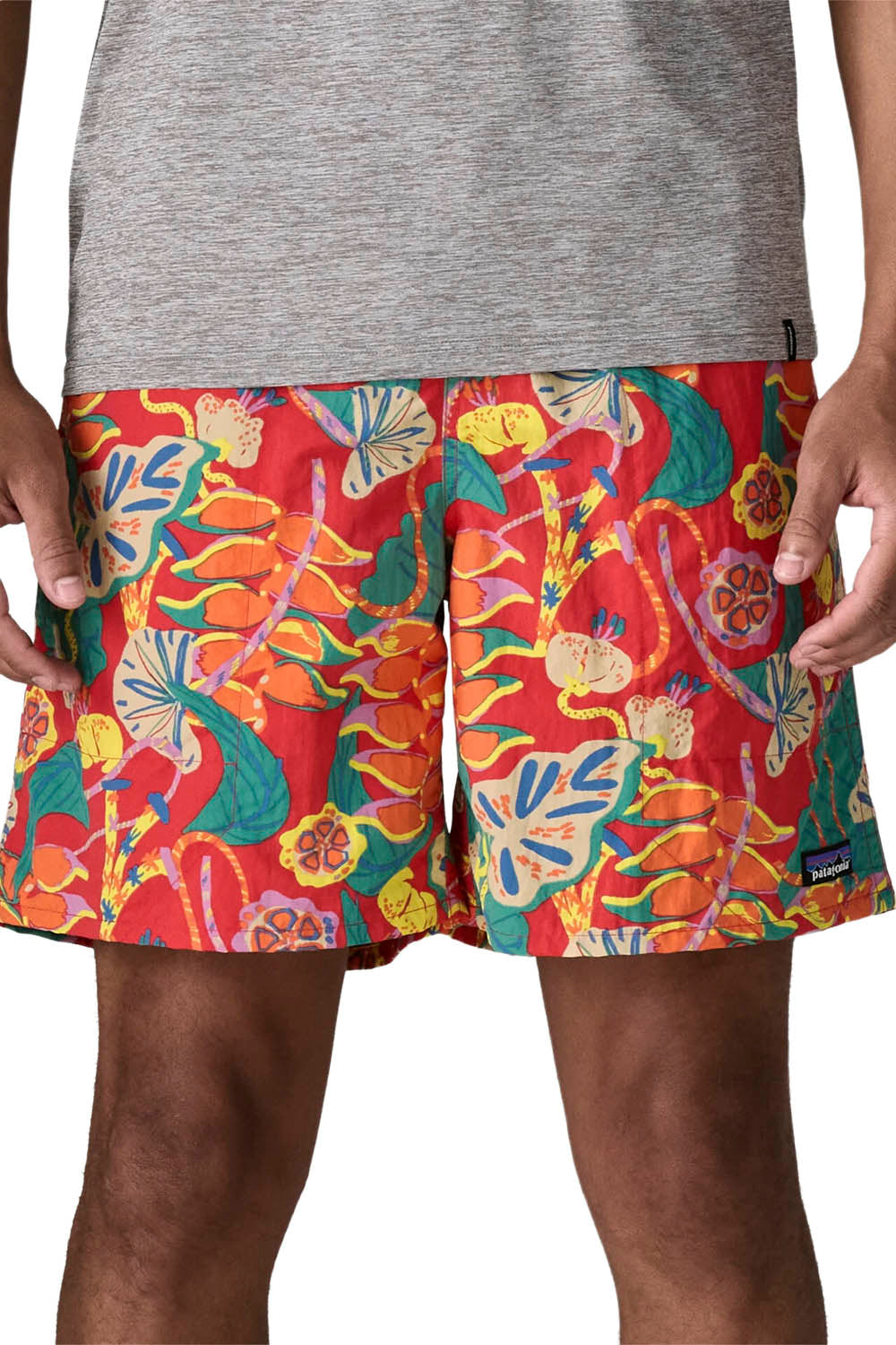 Men's swim trunks featuring a vibrant tropical floral and leaf print in red, orange, yellow, and green, worn by a model with a heather gray t-shirt.