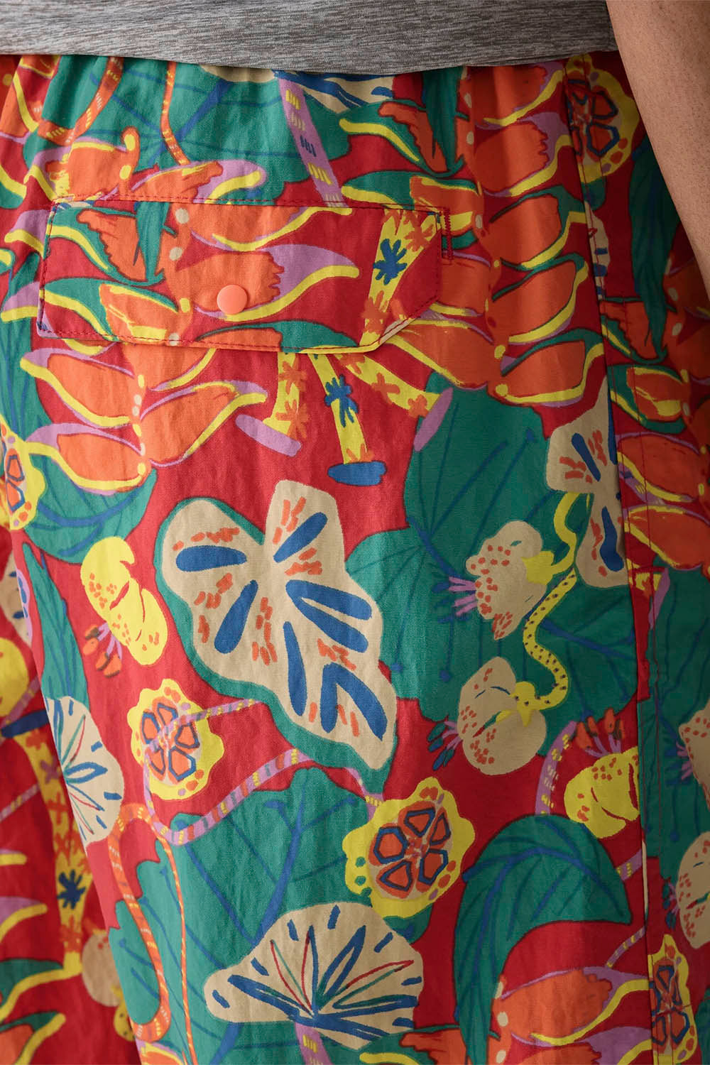 Close-up of a colorful patterned garment, likely a skirt, featuring a vibrant tropical floral print in red, green, yellow, orange, and blue.