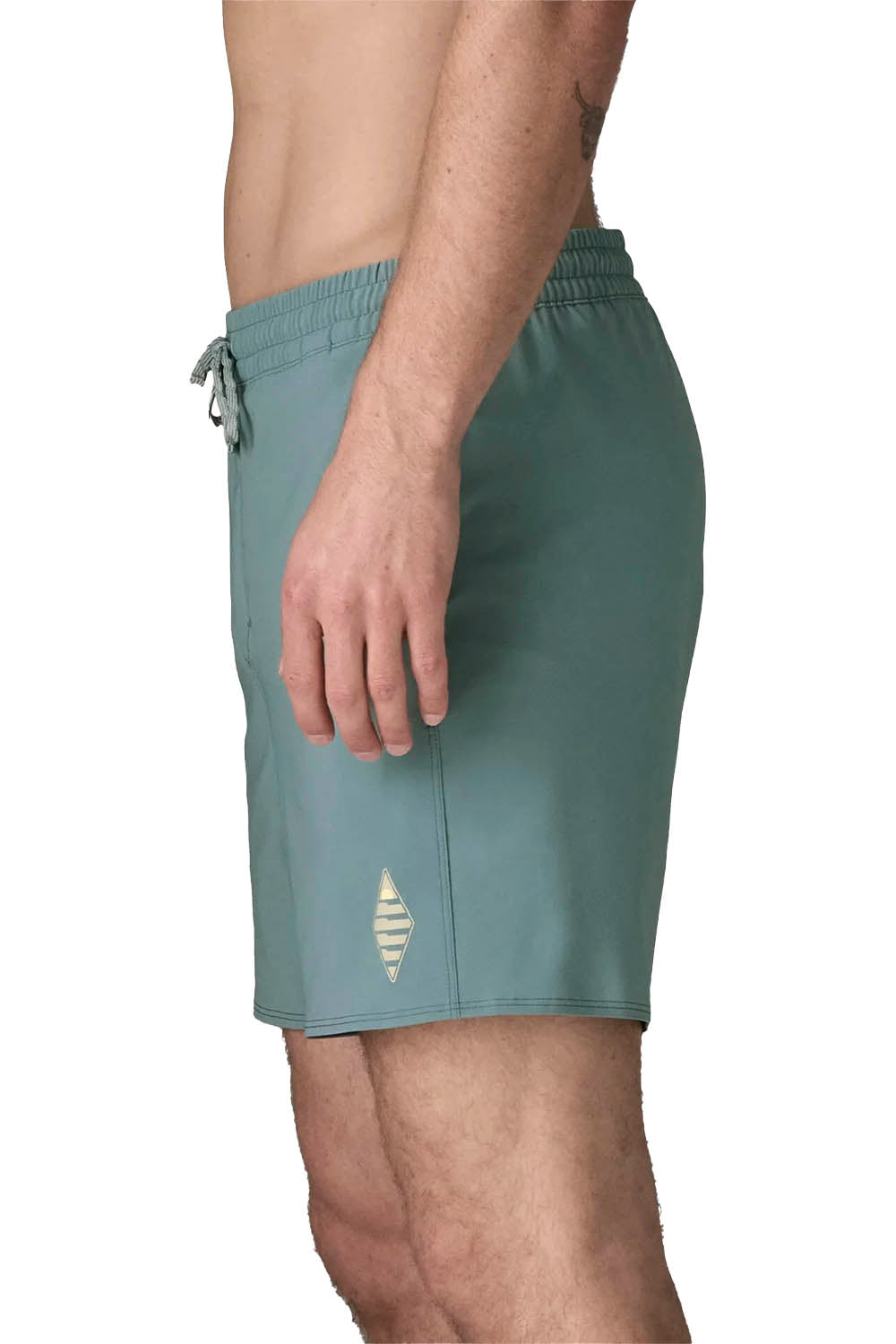 A side view of a man wearing slate blue swim trunks with a small gold geometric logo near the hem, shown against a plain white background.