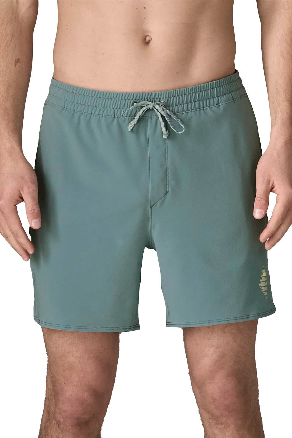 A close-up of a person wearing muted sage green drawstring swim trunks against a plain white background.