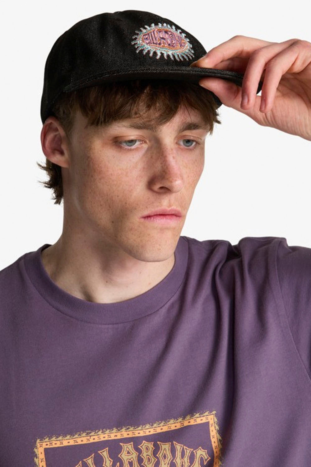 Person wearing a black cap with a decorative emblem and a purple shirt.