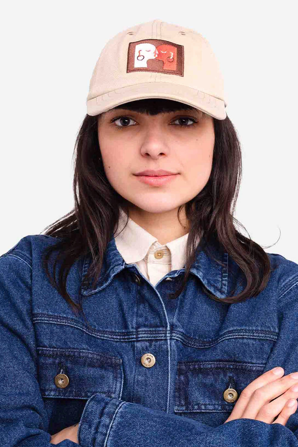 Person wearing a beige cap with a logo and a blue denim jacket on a white background