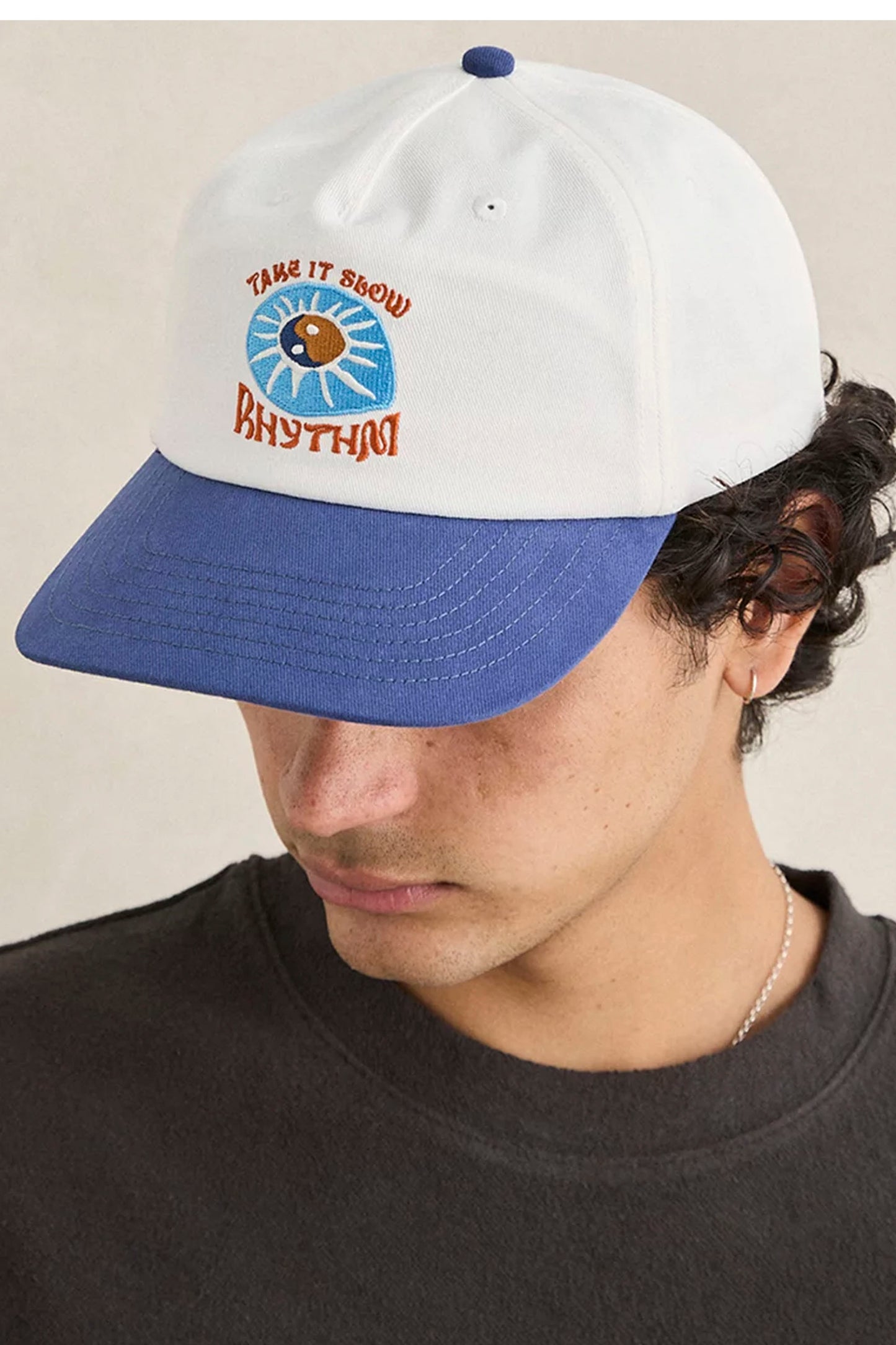 Person wearing Rhythm Slow Down cap with a logo and text on a neutral background