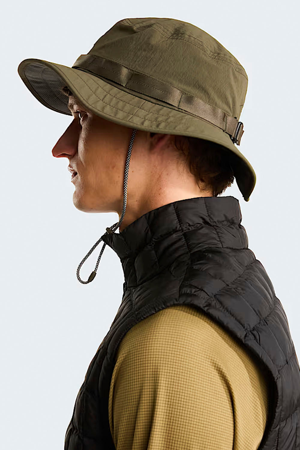Person wearing a green bucket hat and black vest on a white background
