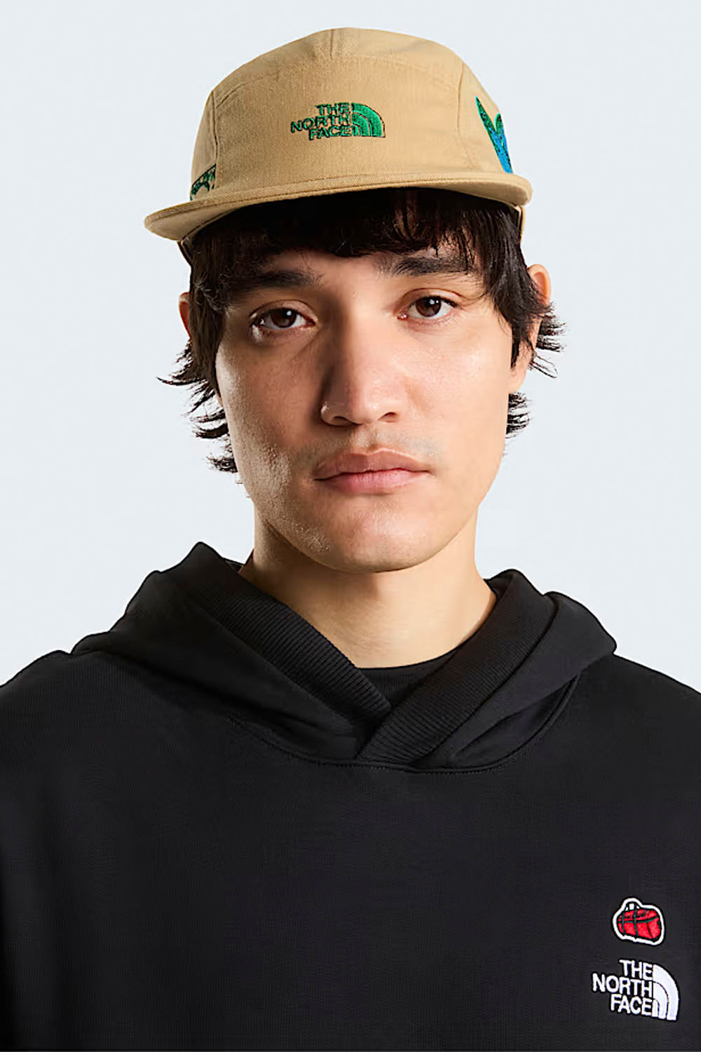 Person wearing a beige cap and black hoodie with The North Face logo on a light gray background