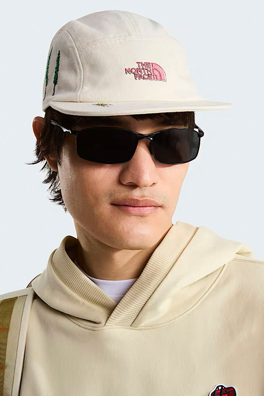 Person wearing a beige cap and sunglasses with a neutral background
