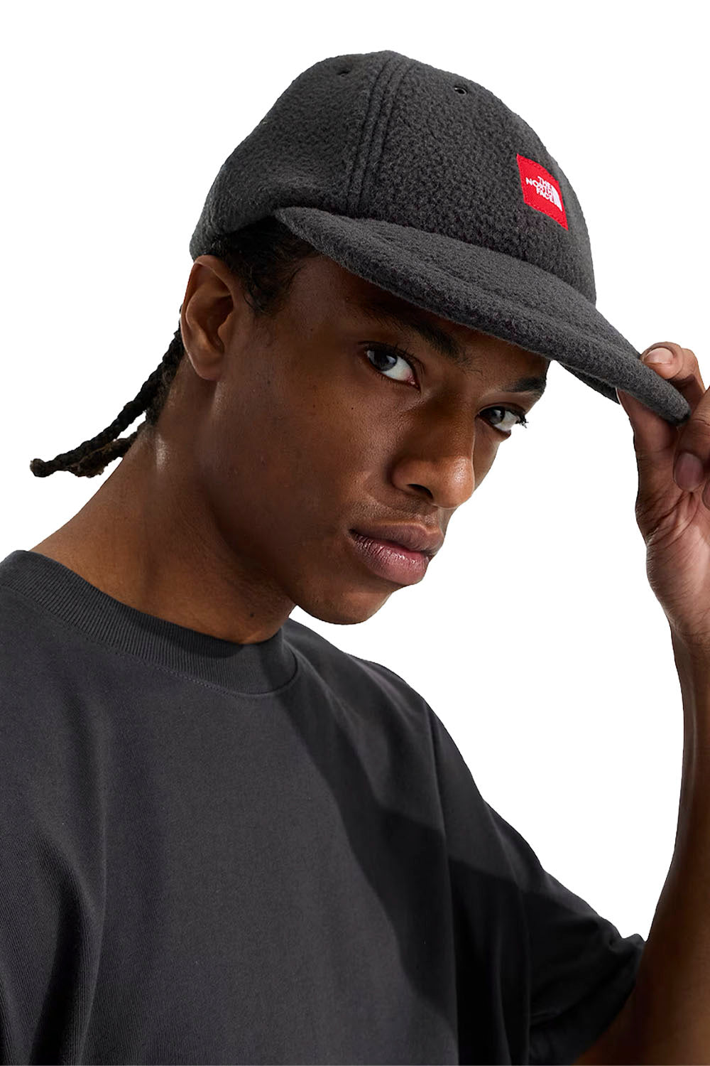A man wearing a dark gray textured fleece 5-panel cap with a small red Supreme box logo on the front, holding the brim with his hand against a white background.