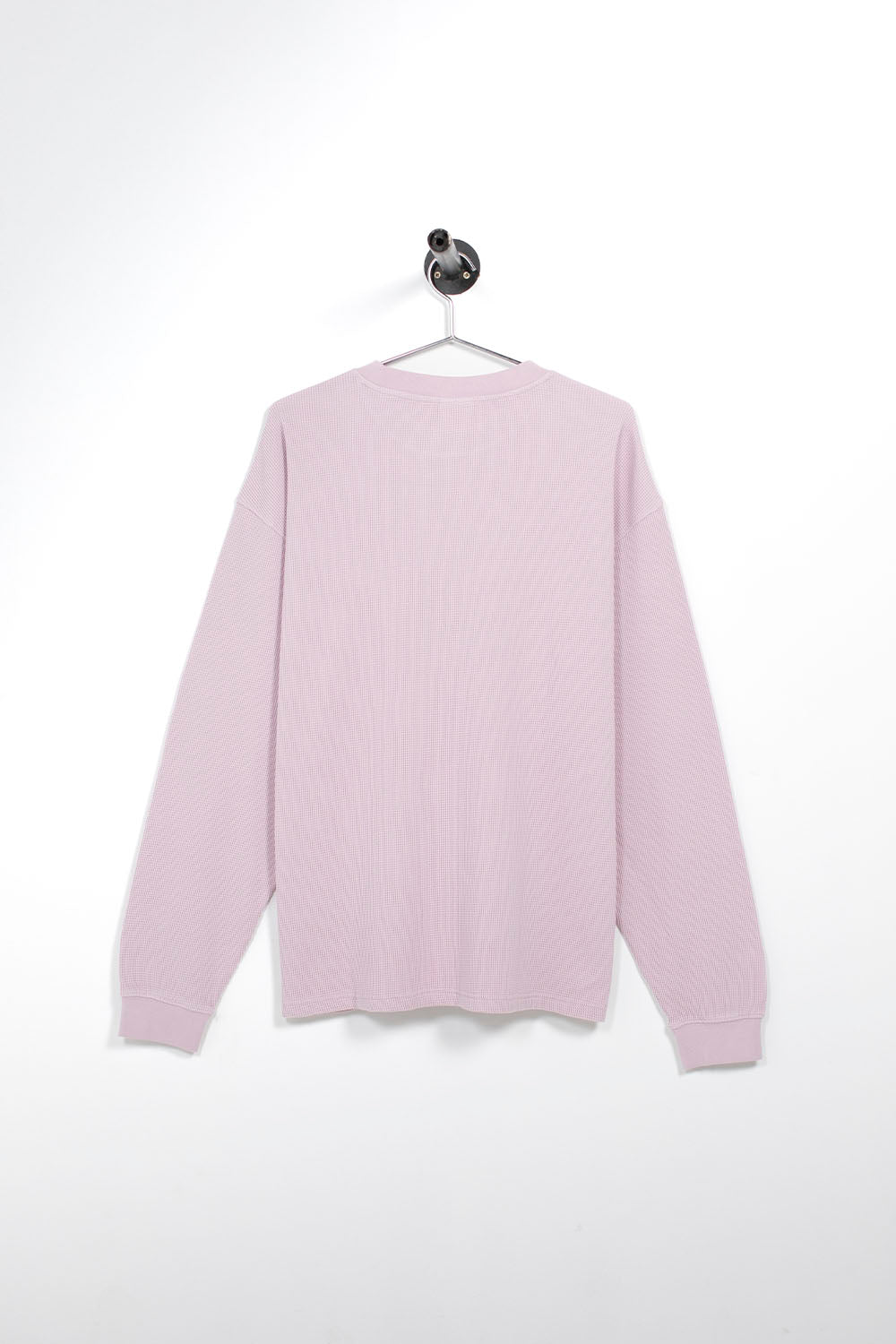 A light pink ribbed knit sweater hanging on a metal hanger against a plain white wall.