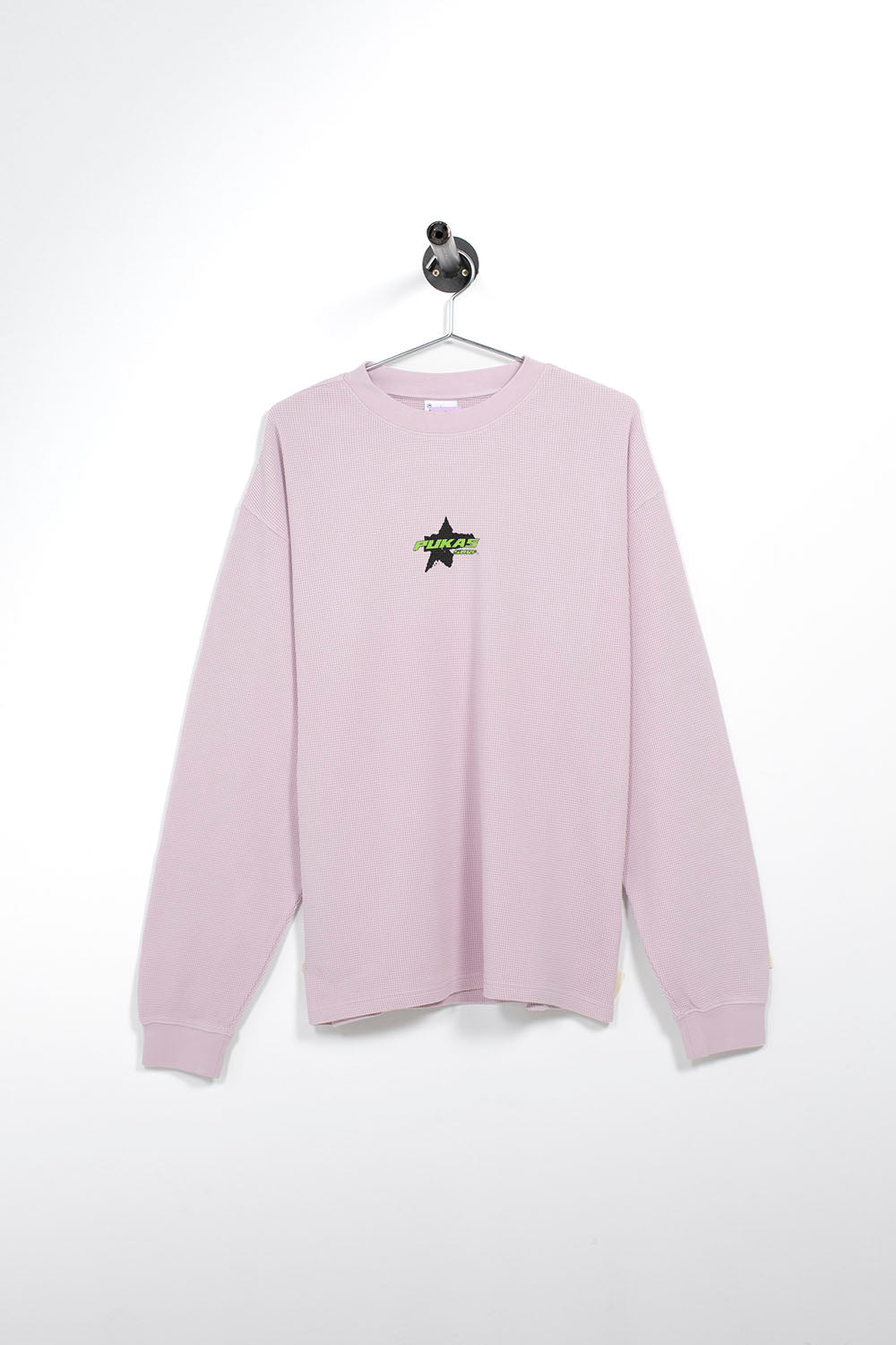 A light pink long-sleeve crewneck sweatshirt hanging on a metal hanger against a white wall. The sweatshirt features a small graphic on the left chest depicting a black star with green and yellow text that reads 'STAY UP LATE'.