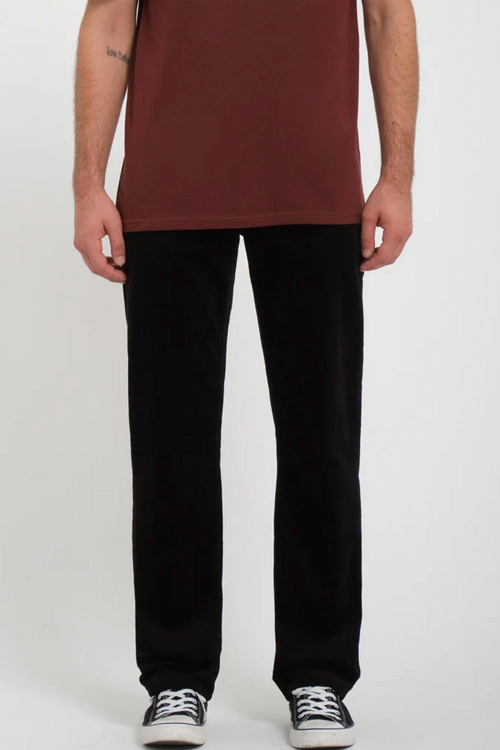 A person wearing black straight-leg sweatpants and a rust-brown tank top, standing against a light gray studio background.