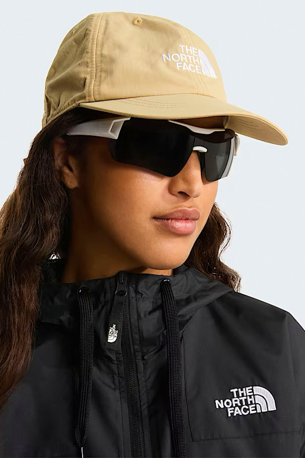 Person wearing a beige cap and black jacket with The North Face logo on a light gray background