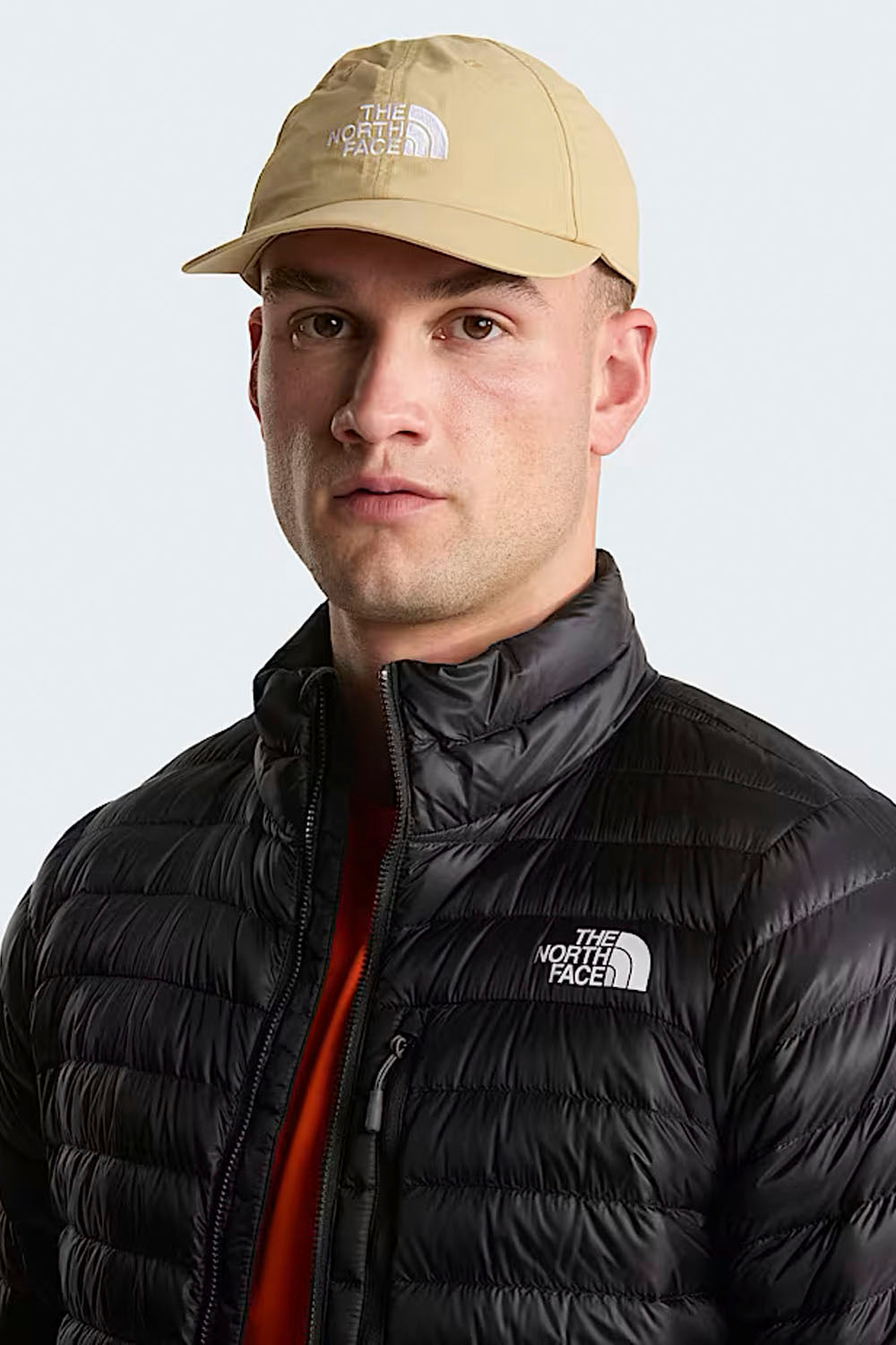 Person wearing a beige cap and black jacket with The North Face logo on a light gray background