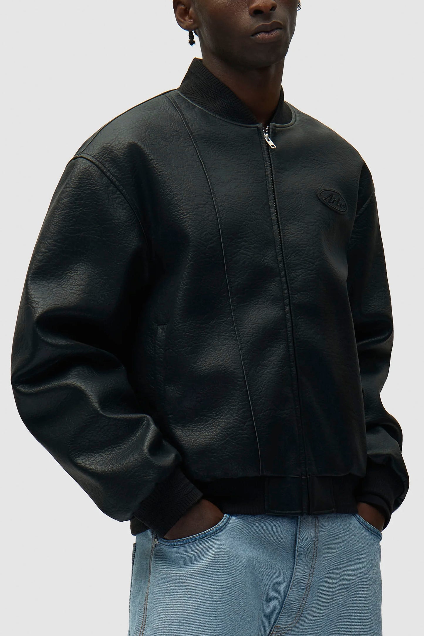 Person wearing a black ARTE leather varsity jacket and light blue jeans on a white background