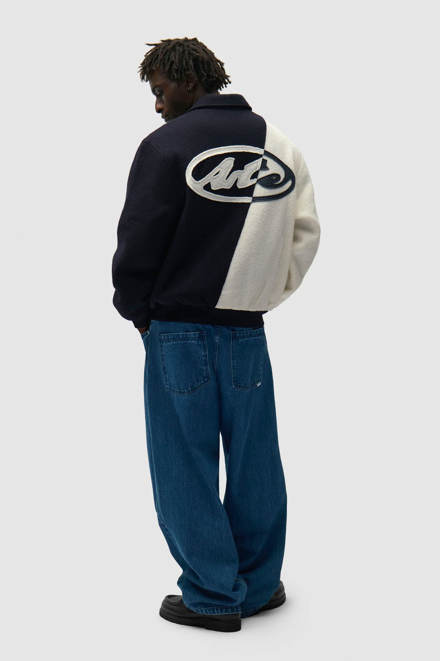 Person wearing a bblue and white ARTE wool Varsity jacket with a logo on the back, standing against a white background