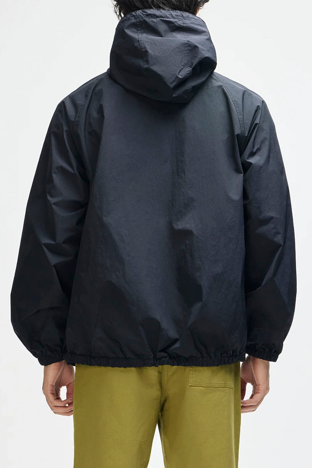 A person shown from the back wearing a dark navy hooded jacket and olive green pants against a plain light gray studio background.
