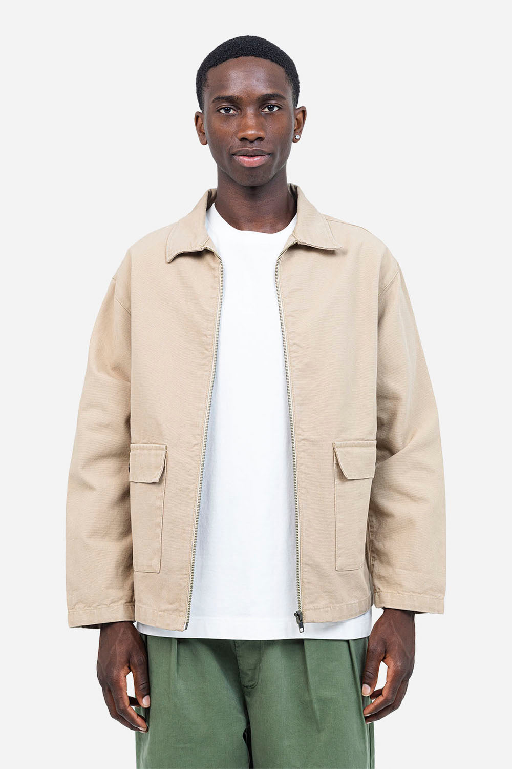 Man wearing a beige jacket over a white shirt with green pants on a white background