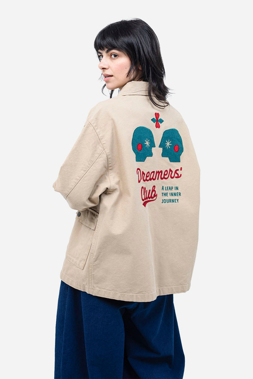 Person wearing a beige jacket with 'Dreamers Club' design on a white background