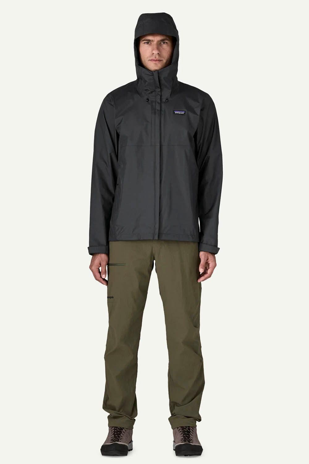 A man wearing a dark gray Patagonia hooded jacket and olive green pants, standing against a light gray background.