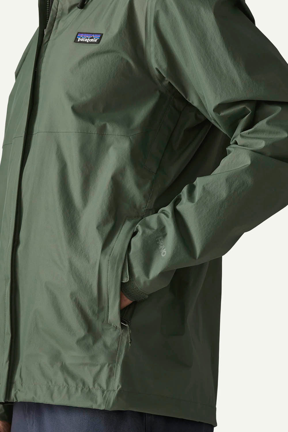 Close-up of a person wearing a Patagonia jacket in olive green, showing the chest logo, sleeve, and side pocket.