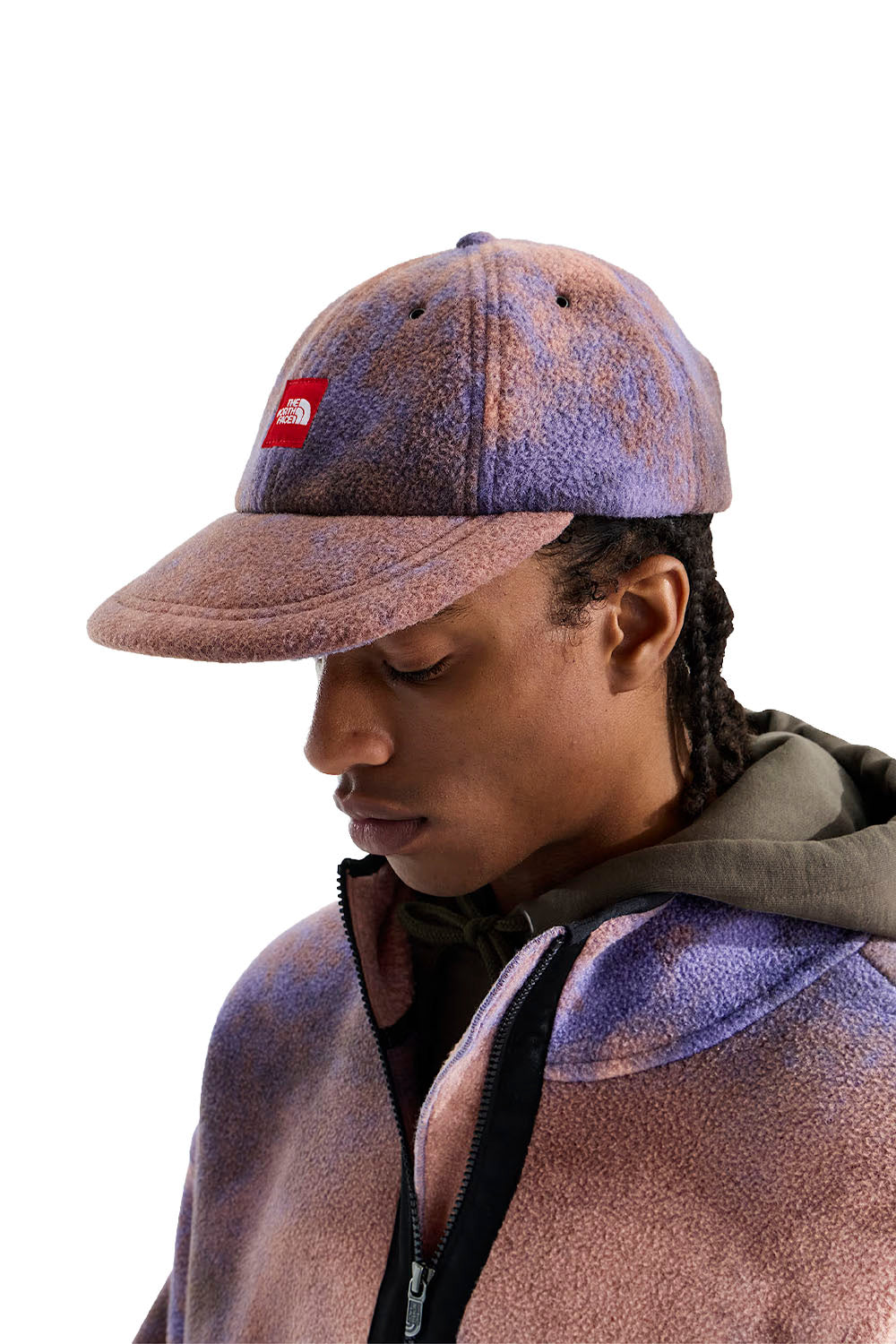A person shown in profile wearing a textured fleece cap and matching zip-up hoodie. The fleece has a mottled purple and dusty rose colorway, and the cap features a small red embroidered The North Face logo on the front.