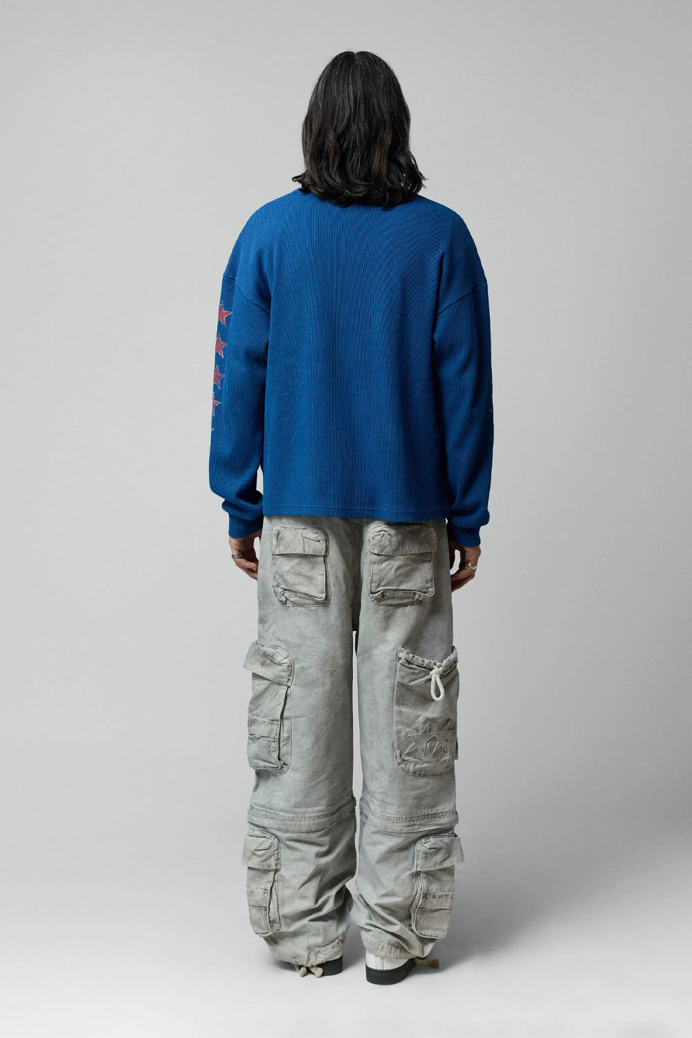 A model shown from the back wearing a blue ribbed knit sweater and light gray wide-leg cargo pants against a neutral gray background.