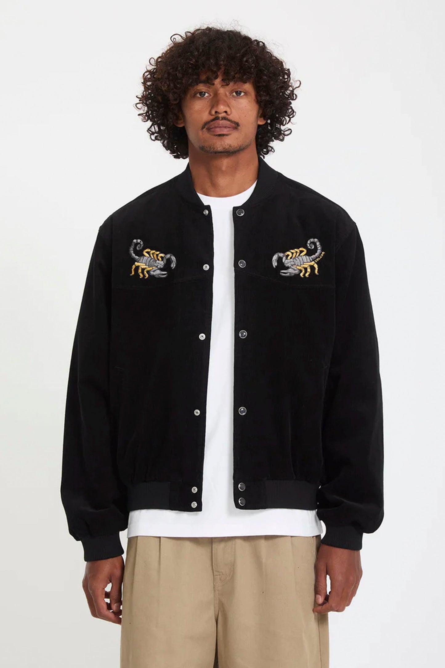 Man wearing a black VOLCOM Fa Mickey Mason jacket with embroidered designs on a white background