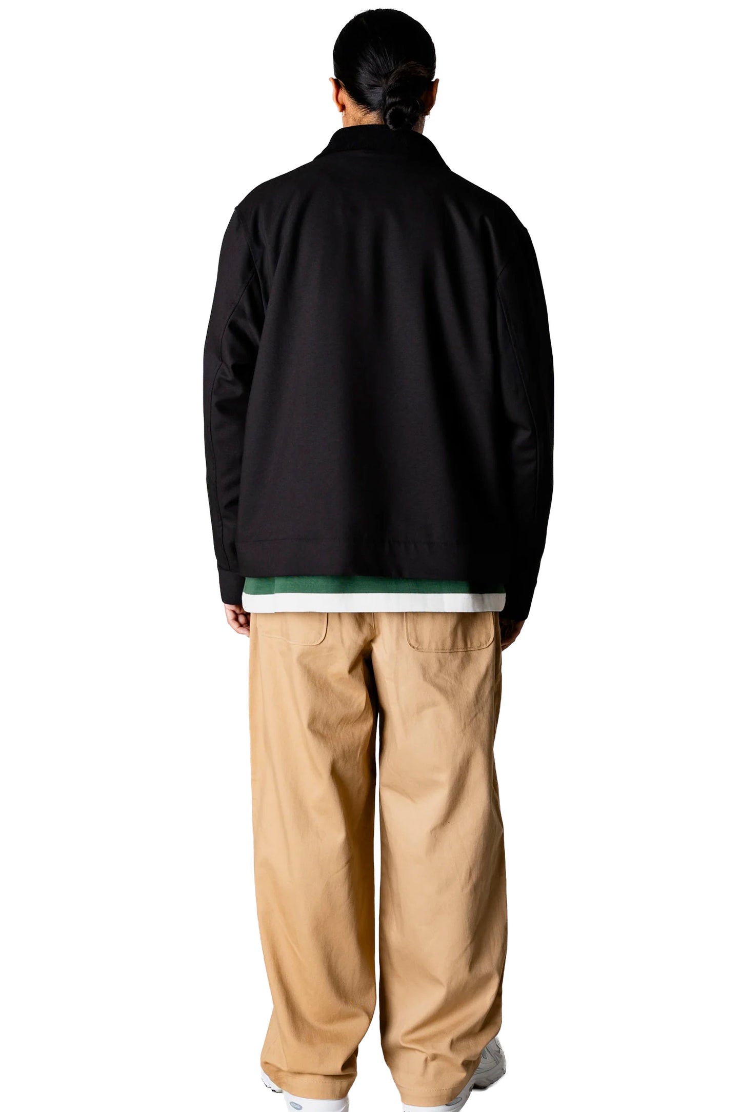 Person wearing a black Woodbird Wbpon Guan Work jacket, striped shirt, beige pants, and white sneakers on a white background