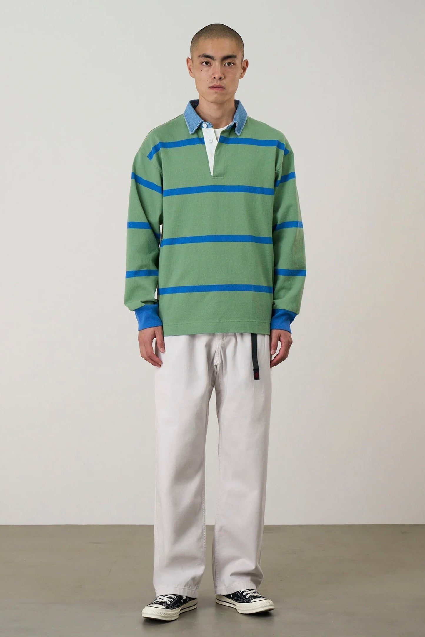 Person wearing a green and blue striped sweater with Light gray Gramicci pants on a plain background