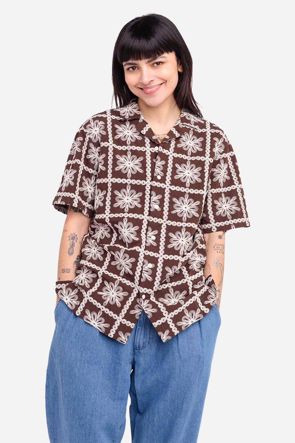 Woman wearing a patterned brown shirt and blue pants on a white background